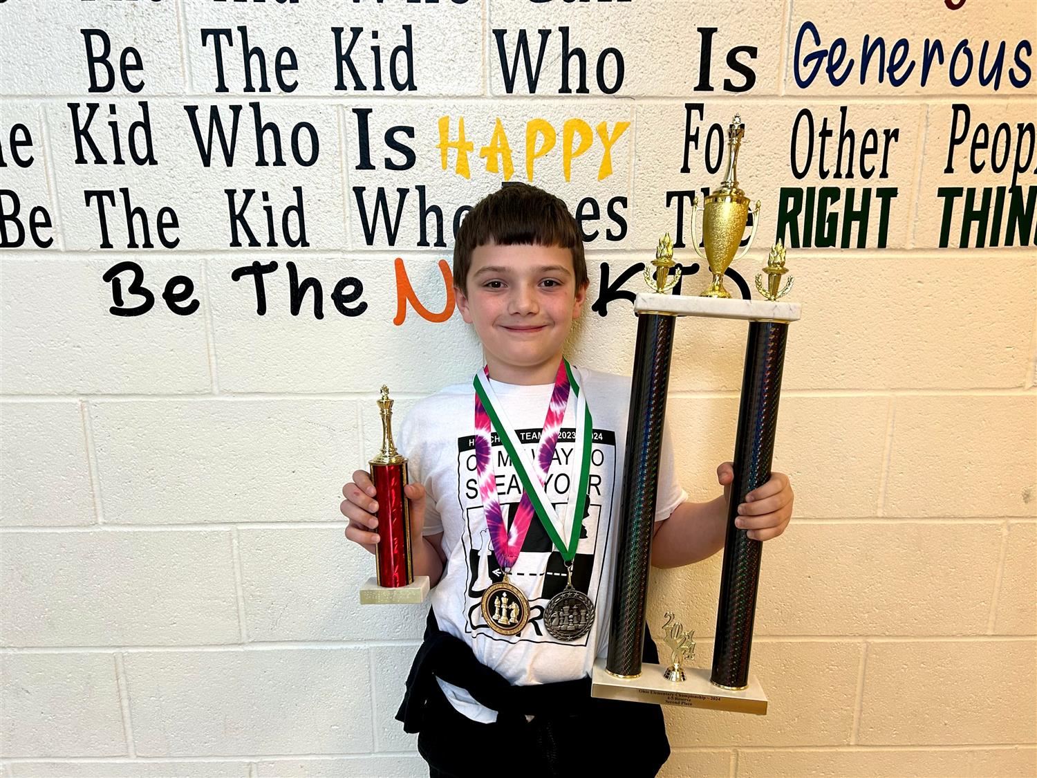 student holding two trophies and two medals in hand