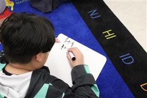student writing math problems on white board